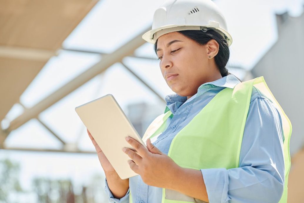 建築現場でタブレットを操作する職人と表示された工程表